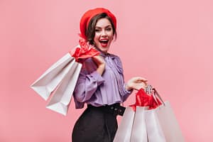 woman red hat black trousers light blouse laughs poses with packages after shopping scaled